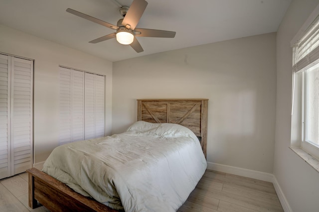 bedroom with light hardwood / wood-style flooring, ceiling fan, and two closets