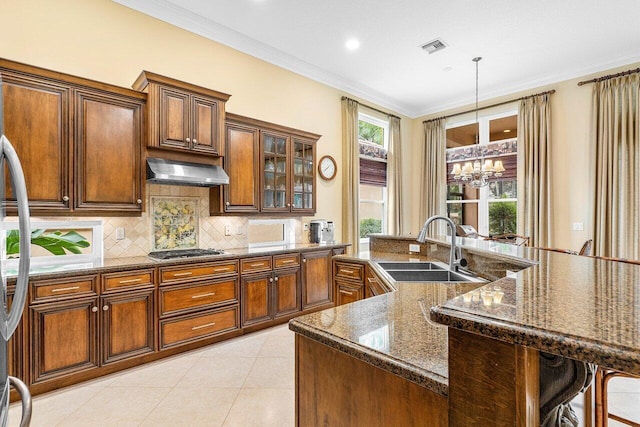 kitchen with sink, hanging light fixtures, crown molding, extractor fan, and a kitchen island with sink