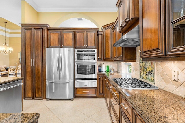 kitchen featuring appliances with stainless steel finishes, ornamental molding, wall chimney exhaust hood, an inviting chandelier, and hanging light fixtures