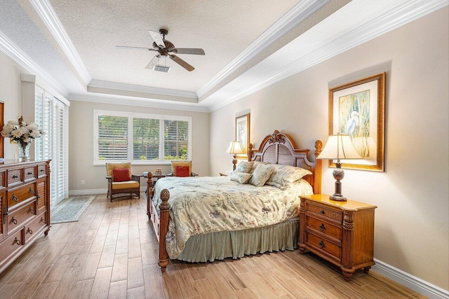 bedroom featuring crown molding, ceiling fan, light wood-type flooring, a textured ceiling, and a tray ceiling