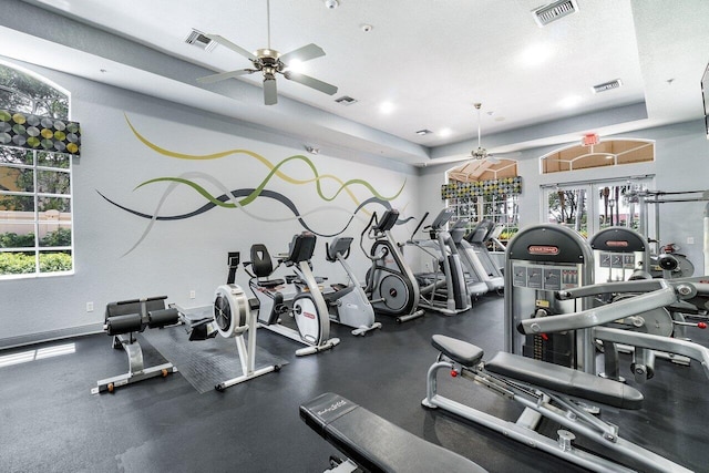 exercise room featuring a textured ceiling, a raised ceiling, ceiling fan, and a healthy amount of sunlight