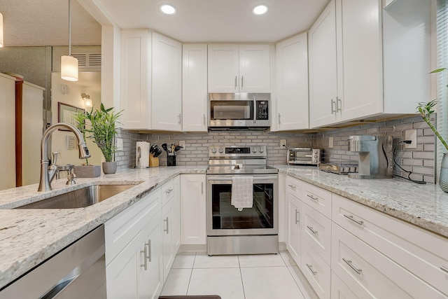 kitchen with stainless steel appliances, sink, light tile patterned floors, white cabinets, and pendant lighting