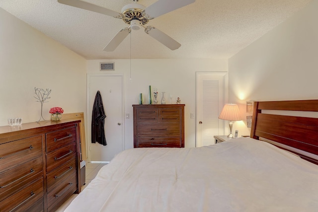 tiled bedroom with ceiling fan, a textured ceiling, and a closet