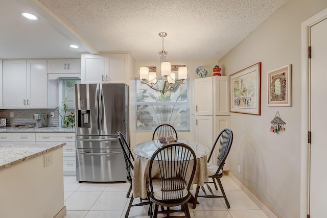 tiled dining space with a textured ceiling and an inviting chandelier