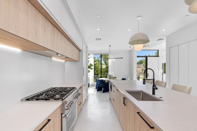 kitchen with light brown cabinetry, stainless steel range, hanging light fixtures, and sink