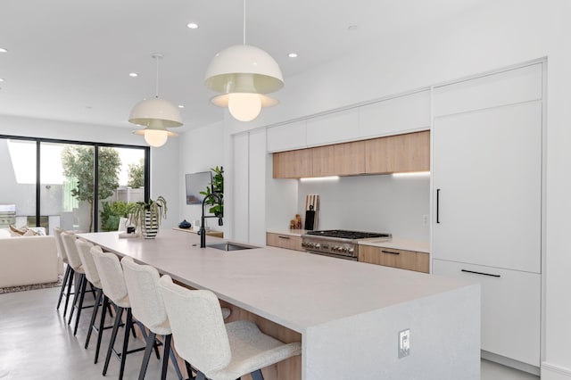 kitchen featuring white cabinets, sink, stainless steel range oven, and an island with sink