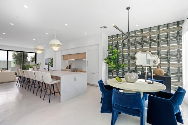 kitchen with sink, white cabinetry, hanging light fixtures, and a kitchen island with sink