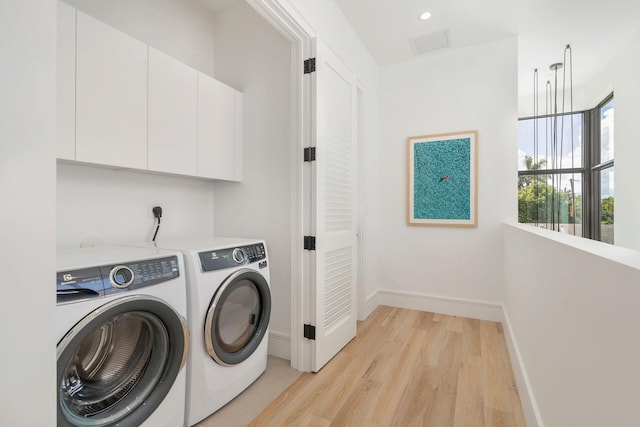 laundry area featuring washing machine and dryer, cabinets, and light wood-type flooring