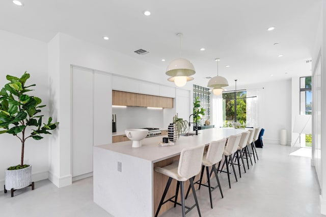 kitchen featuring a breakfast bar, a center island with sink, white cabinets, and decorative light fixtures