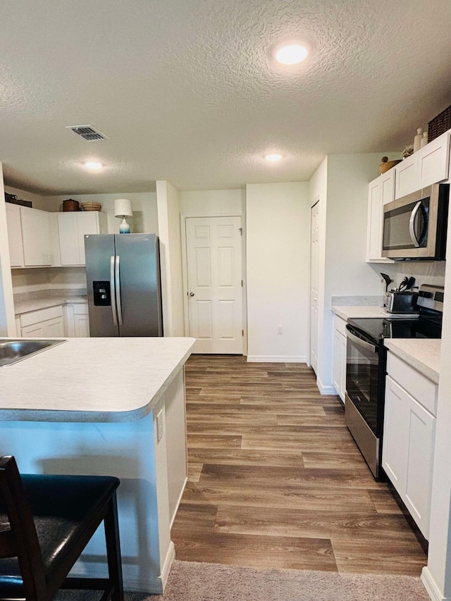 kitchen featuring a textured ceiling, stainless steel appliances, white cabinetry, and hardwood / wood-style flooring