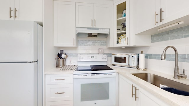 kitchen with light stone counters, decorative backsplash, sink, white cabinetry, and white appliances