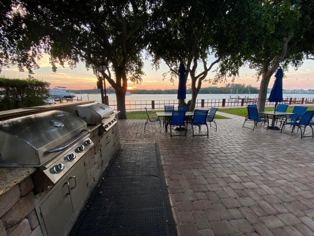 patio terrace at dusk featuring area for grilling, a grill, and a water view