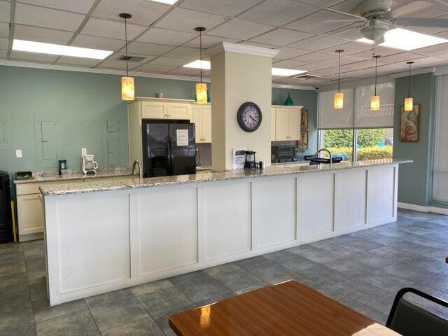 kitchen featuring white cabinetry, light stone countertops, decorative light fixtures, and black refrigerator