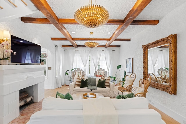 living room featuring beam ceiling, a chandelier, a textured ceiling, a tiled fireplace, and light wood-type flooring