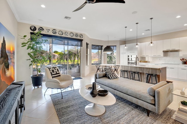 tiled living room featuring ceiling fan, sink, and ornamental molding