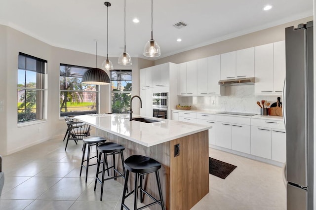 kitchen with appliances with stainless steel finishes, sink, pendant lighting, white cabinets, and an island with sink