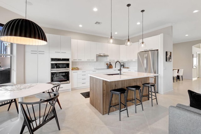 kitchen with white cabinets, sink, light tile patterned flooring, an island with sink, and backsplash