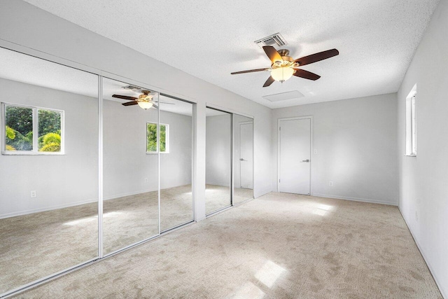 unfurnished bedroom featuring multiple windows, two closets, ceiling fan, and light colored carpet