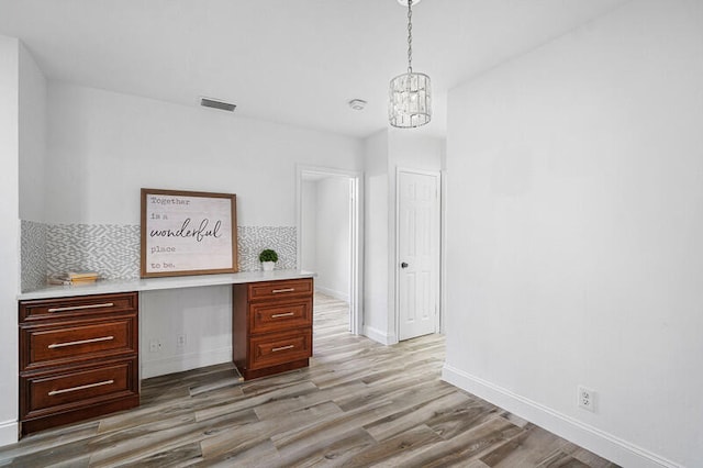 unfurnished office featuring built in desk, a notable chandelier, and light wood-type flooring