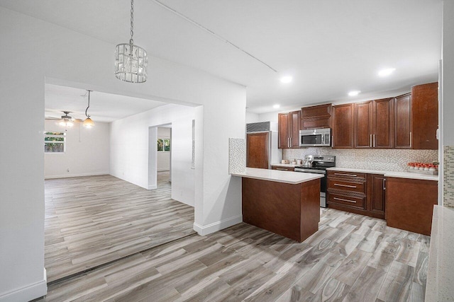 kitchen with backsplash, appliances with stainless steel finishes, decorative light fixtures, light hardwood / wood-style floors, and kitchen peninsula