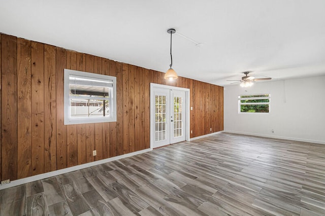 unfurnished room featuring hardwood / wood-style floors, a healthy amount of sunlight, wooden walls, and french doors