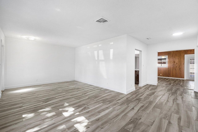 spare room featuring wooden walls, light hardwood / wood-style flooring, and a textured ceiling