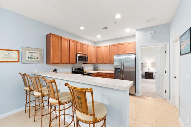 kitchen with kitchen peninsula, appliances with stainless steel finishes, light tile patterned floors, and a breakfast bar area