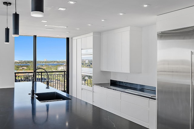 kitchen featuring dark countertops, white cabinets, stainless steel built in fridge, and decorative light fixtures