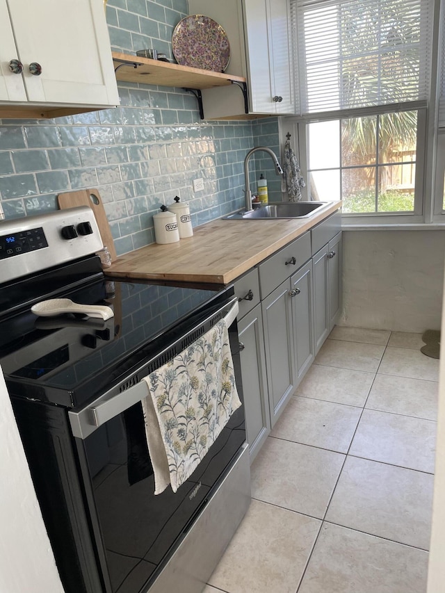 kitchen with stainless steel range with electric cooktop, butcher block counters, light tile patterned floors, gray cabinets, and sink