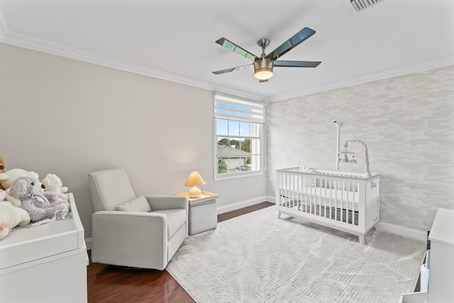 bedroom with ceiling fan, dark hardwood / wood-style floors, a crib, and ornamental molding