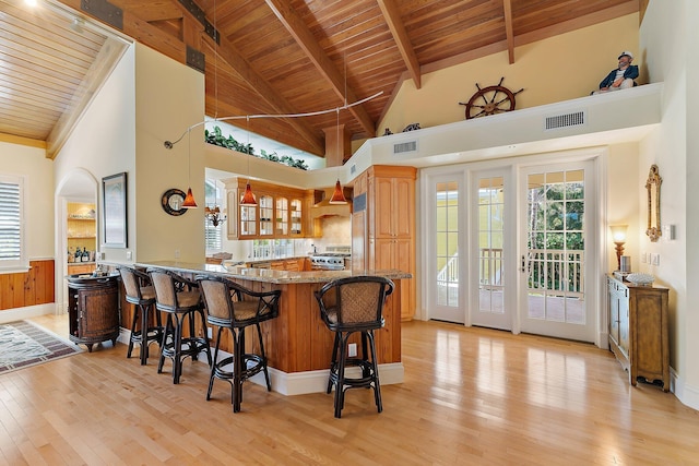 kitchen with high vaulted ceiling, kitchen peninsula, dark stone counters, light hardwood / wood-style floors, and a breakfast bar area