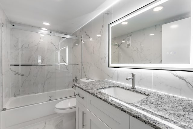 full bathroom with vanity, toilet, tile walls, and bath / shower combo with glass door