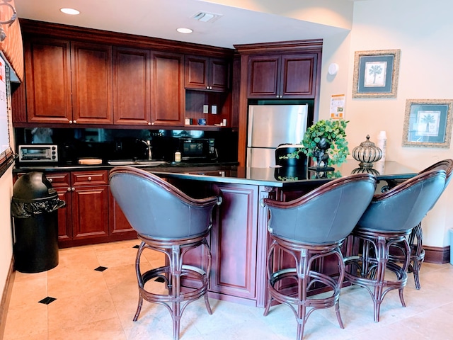 kitchen with backsplash, sink, stainless steel fridge, light tile patterned floors, and a kitchen bar