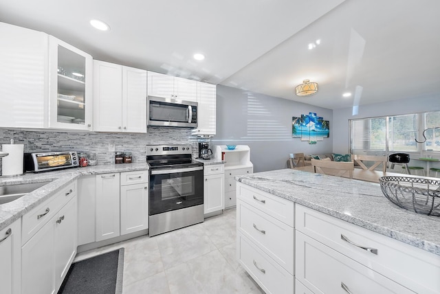 kitchen with stainless steel appliances, sink, tasteful backsplash, light stone countertops, and white cabinetry