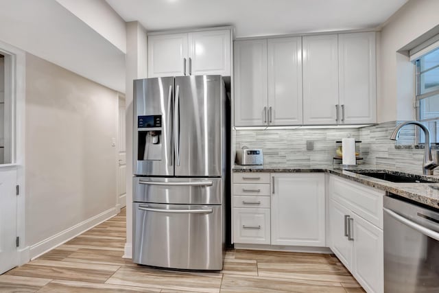 kitchen with appliances with stainless steel finishes, a sink, tasteful backsplash, light wood finished floors, and dark stone countertops