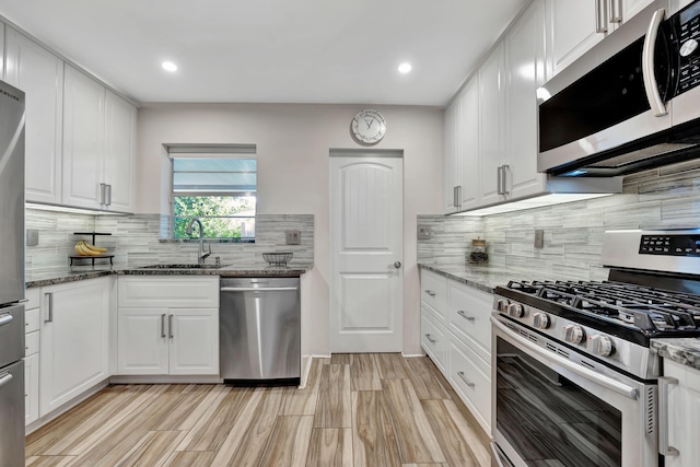 kitchen featuring stainless steel appliances, a sink, white cabinetry, tasteful backsplash, and dark stone countertops
