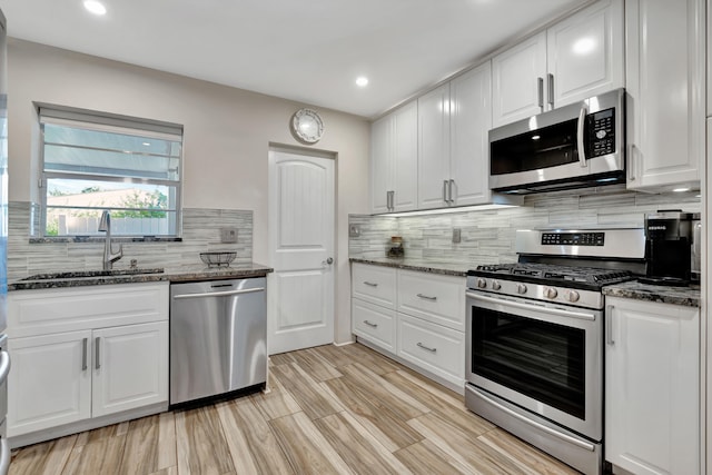 kitchen with stainless steel appliances, white cabinetry, sink, and dark stone counters