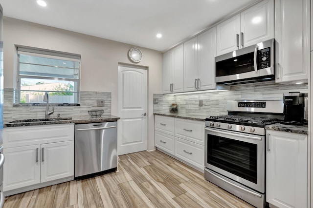 kitchen with appliances with stainless steel finishes, a sink, white cabinetry, dark stone countertops, and recessed lighting
