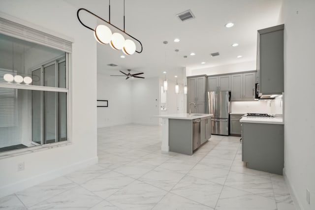 kitchen with stainless steel appliances, a center island with sink, decorative light fixtures, and gray cabinetry