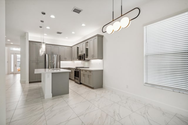 kitchen with pendant lighting, sink, gray cabinets, appliances with stainless steel finishes, and an island with sink