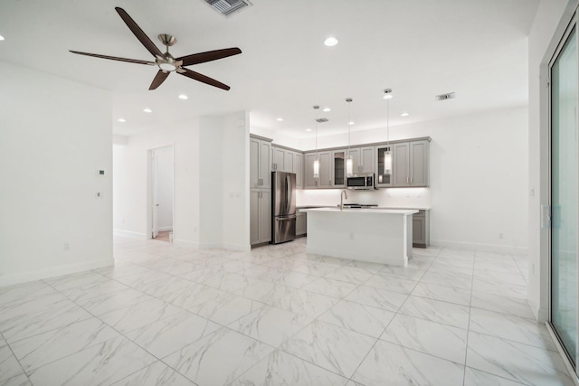 kitchen with appliances with stainless steel finishes, decorative light fixtures, gray cabinets, ceiling fan, and a kitchen island with sink