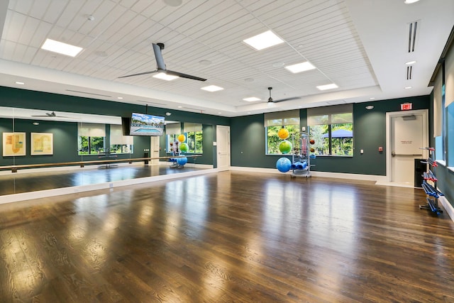 exercise room featuring ceiling fan, a healthy amount of sunlight, a raised ceiling, and wood-type flooring