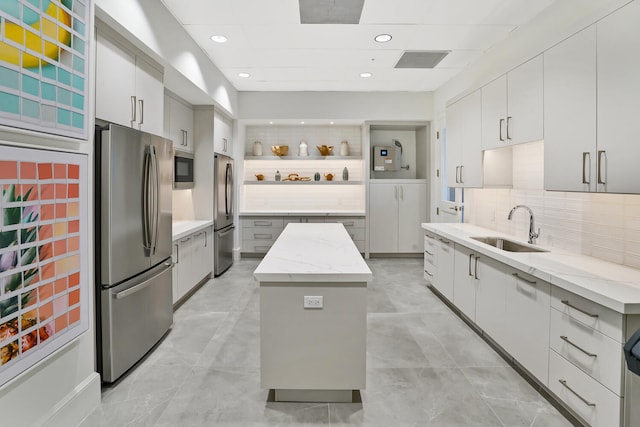 kitchen featuring a kitchen island, backsplash, appliances with stainless steel finishes, light stone countertops, and sink