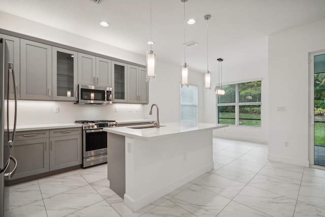 kitchen with gray cabinets, sink, hanging light fixtures, stainless steel appliances, and a center island with sink