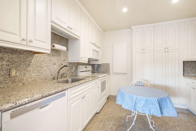 kitchen with sink, light stone counters, stainless steel dishwasher, white cabinets, and electric range