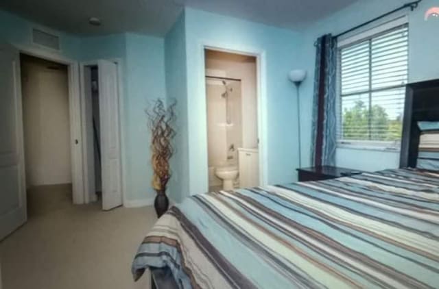 bedroom featuring ensuite bathroom and light colored carpet