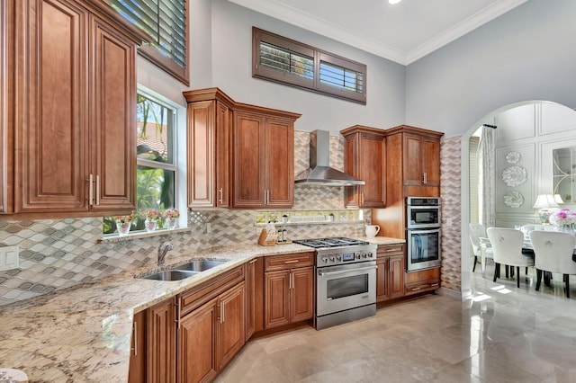 kitchen featuring stainless steel appliances, light stone counters, ornamental molding, backsplash, and wall chimney range hood