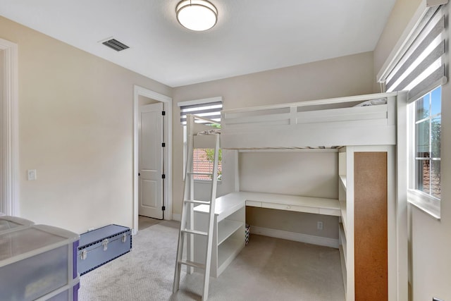 carpeted bedroom with built in desk and multiple windows