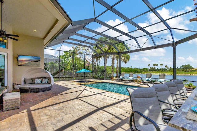 view of pool featuring glass enclosure, a patio area, a water view, and ceiling fan