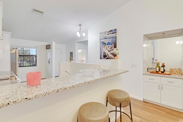 kitchen featuring a kitchen bar, white cabinets, stainless steel refrigerator, light hardwood / wood-style flooring, and decorative light fixtures